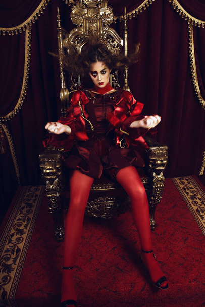 Femme habillée comme la reine des cœurs, maquillage créatif avec un grand cœur sur les yeux, fille assise sur le trône, portrait retouché hi-end. Photo conceptuelle
 - Photo, image