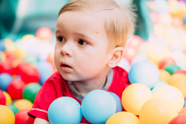Gülen çocuk 1-2 yaşında, çocuk parkında ve oyun merkezinde doğum günü partisinde top havuzunda eğleniyor. Çocuk oyun parkında renkli toplarla oynuyor. Küçük çocuk için oyuncaklar. - Fotoğraf, Görsel