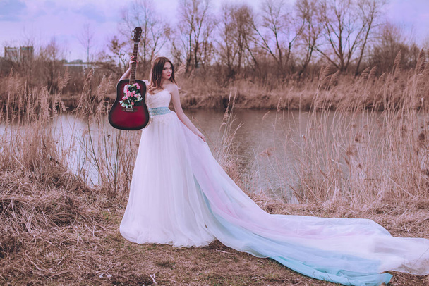Menina europeia romântica bonita com guitarra com flores dentro, posando ao ar livre. Conceito de música e natureza. Hora da Primavera. Moda retocada tiro
 - Foto, Imagem