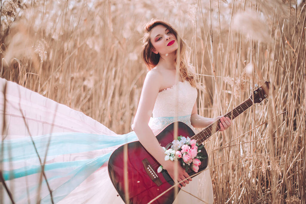 Krásná romantická evropská dívka s kytarou s květinami uvnitř, pózující venku. Pojem hudba a příroda. Jaro. Módní retušovaný výstřel - Fotografie, Obrázek