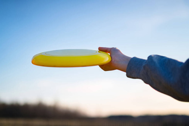 Mão segurando frisbee amarelo lá fora. Jogando frisbee ao ar livre com céu azul no fundo
 - Foto, Imagem