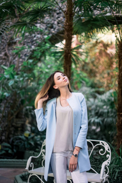 The young elegant positive girl poses in a botanical garden wearing blue jacket. - Fotoğraf, Görsel