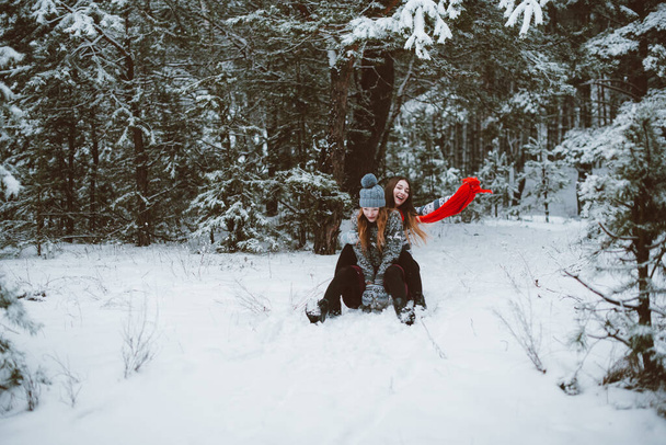 Twee jonge hippe hippe vriendinnen samen. Close-up modeportret van twee zusjes knuffels en hebben plezier in de winter, het dragen van een trui, beste vriendinnen paar buiten, besneeuwd weer - Foto, afbeelding