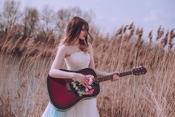 Όμορφη ρομαντική ευρωπαϊκή κοπέλα με κιθάρα με λουλούδια στο εσωτερικό, ποζάροντας σε εξωτερικούς χώρους. Έννοια της μουσικής και της φύσης. Άνοιξη. Μόδας retouched πλάνο - Φωτογραφία, εικόνα