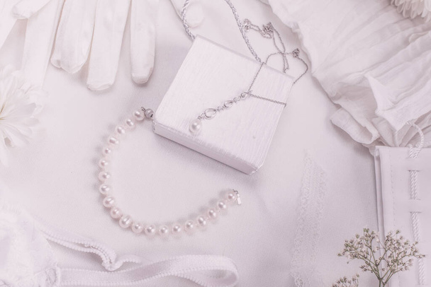 Witte bruids accessoires voor bruiloft achtergrond met parels, witte satijnen linten en kant, handschoenen, armband, platte lay voor mode blog, top view - Foto, afbeelding