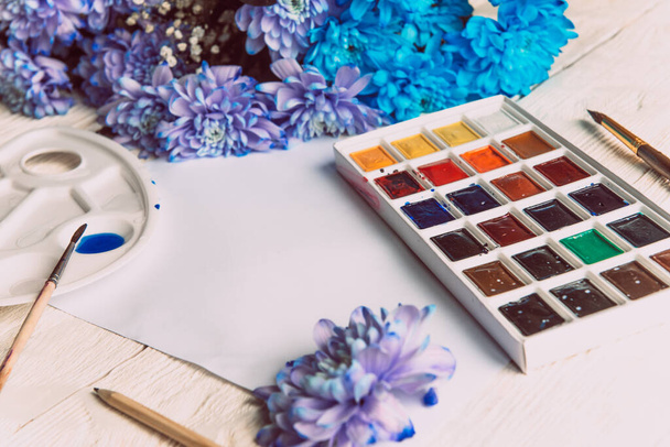 Palette of watercolor paints, brushes and paper for a water color on wooden background, close up. Flat lay, spring background with copy space. - Фото, изображение