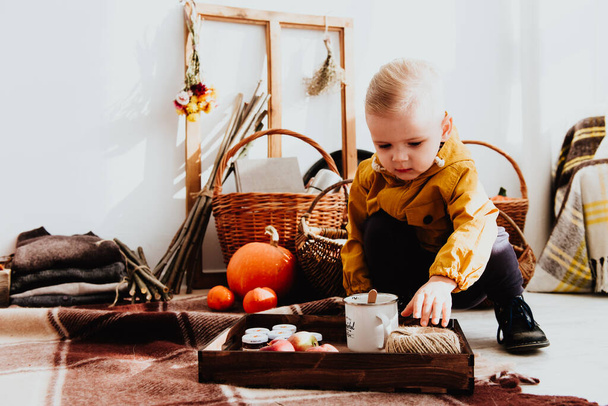 Cool trendy hipster boy 2 years old wears yellow jacket posing at the decorated photozone of autumn decor with beautiful bright autumn leaves. Cosy atmosphere - Photo, Image
