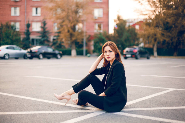 Red-haired model in a suit sits in a parking lot in summer - 写真・画像