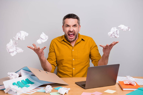 Frustrated angry agent man work home quarantine sit desk cant finish start-up development project crumple paper throw air fly fall scream wear yellow shirt isolated gray color background - Photo, Image