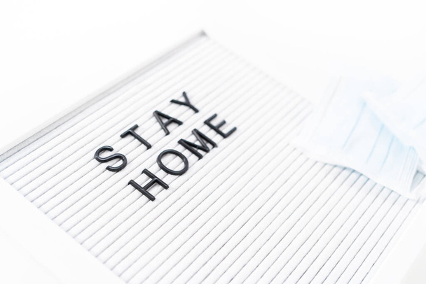Знак STAY HOME на дошці оголошень з синьою медичною маскою
. - Фото, зображення