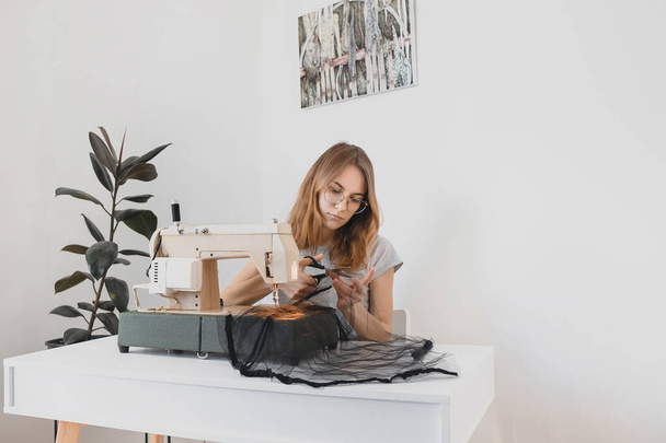 La ragazza Vestito da cucito in tulle di tessuto nero su una macchina da cucire vintage nel posto di lavoro della stanza hobby fatto a mano
 - Foto, immagini