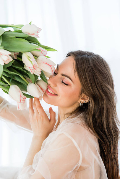 Attractive young woman holding a bouquet of white tulips in her hands on a white background - Foto, imagen