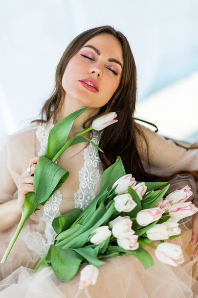 白いチューリップの大きな花束を保持しているドレスでリラックスした若い女性の肖像 - 写真・画像