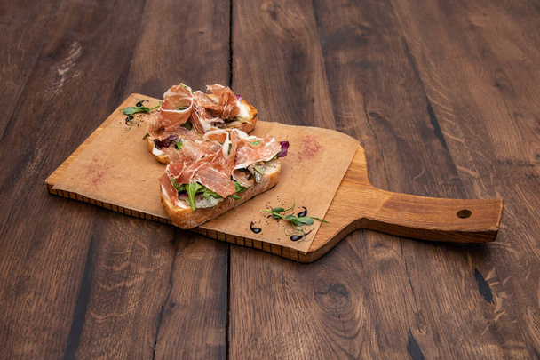 Bruschetta with Parma ham:  Ciabatta, Parma ham, Gorgonzola cheese, hazelnut, pear, grain mustard sauce and mixed salad on a wooden Board. - Fotografie, Obrázek