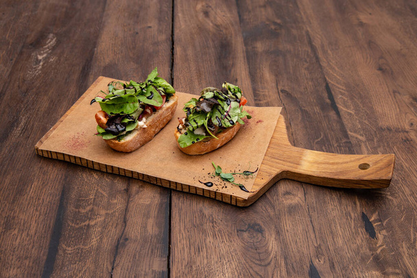 Bruschetta with tomatoes and Basil: Ciabatta, tomatoes, cream cheese, mixed salad, sun-dried tomatoes, balsamic cream sauce, pine nuts on a wooden Board. - Fotografie, Obrázek