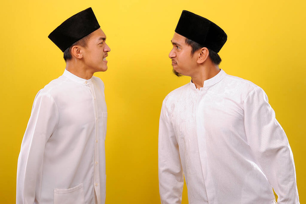 Imagen de dos jóvenes musulmanes asiáticos que se ven furiosos entre sí. Concepto Ramadán. aislado sobre fondo amarillo
 - Foto, Imagen