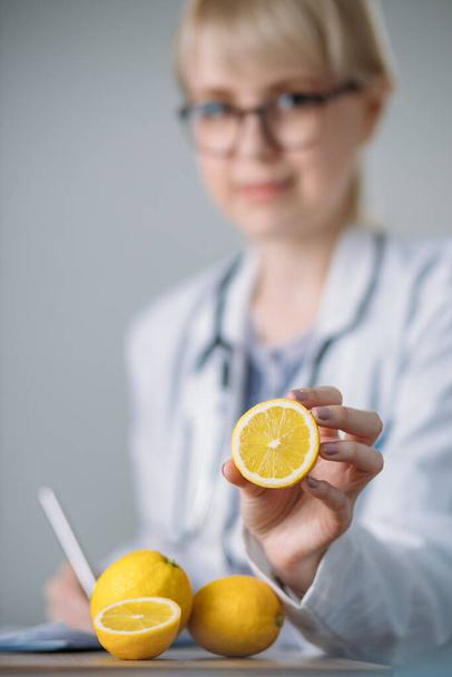 Ärztin verschreibt einer Patientin gesunde Ernährung. Eine Zitrone in der Hand. Zitrone im Fokus. - Foto, Bild