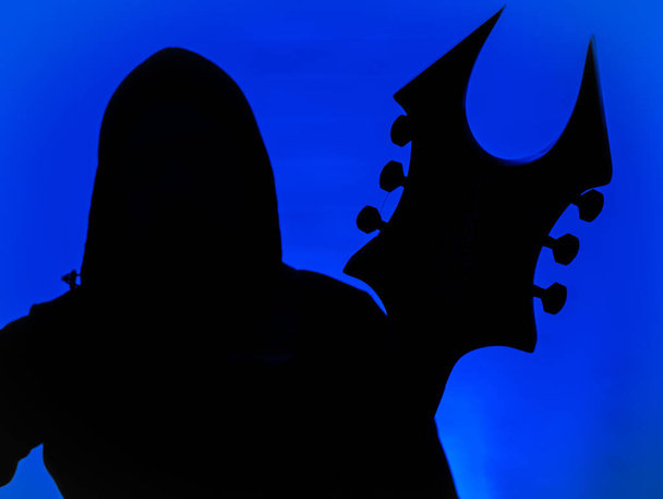 Gitarzysta z kapturem i ostry Heavy Metal gitara z rogaty headstock na niebieskim tle - Zdjęcie, obraz