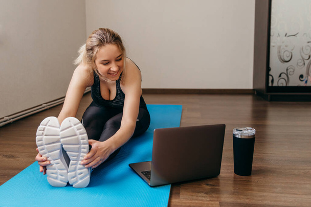 Young woman exercising at home in a living room. Video lesson. Young woman repeating exercises while watching online workout session. Beautiful young woman doing fitness exercise at home - Photo, Image