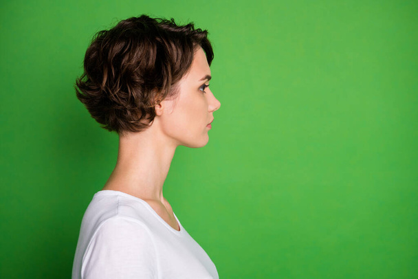 Closeup profile photo of attractive lady short wavy hairdo not smiling look side empty space concentrated wear casual white t-shirt isolated green color background - Foto, afbeelding