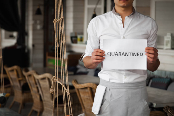 Man in uniform houdt wit vel papier met woord in quarantaine - Foto, afbeelding