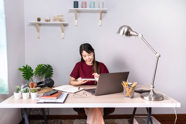 Pensive aziatische vrouw is ontspannen op desktop werken op afstand van huis met laptop voor communiceert op internet met de klant, E leren onderwijzen in online chat, quarantaine Coronavirus concept - Foto, afbeelding