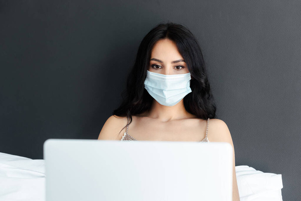 attractive woman in medical mask using laptop in bed on self isolation - Fotoğraf, Görsel