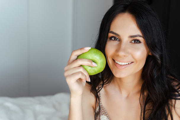 piękne uśmiechnięta dziewczyna gospodarstwa zielone świeże jabłko w sypialni - Zdjęcie, obraz