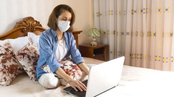 Distance learning online education and work.Happy woman girl working office work remotely from home on bed. using a medical mask - Fotó, kép