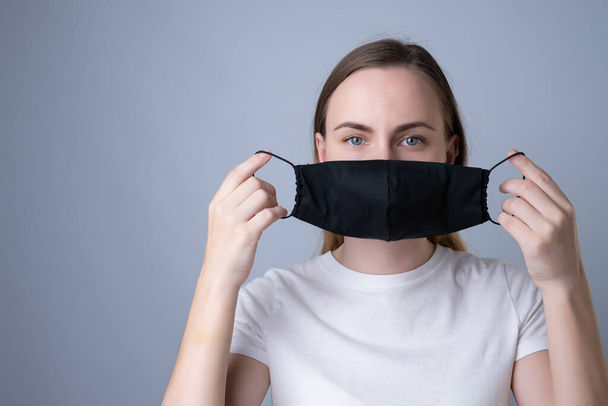 Woman puts a black medical mask on her face on a gray background - Fotografie, Obrázek