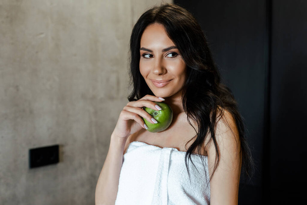 beautiful woman in towel holding apple on kitchen in morning - Φωτογραφία, εικόνα