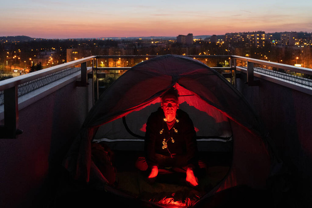 Man is meditating in touristic tent on the balcony of his apartment during coronavirus quarantine - Fotografie, Obrázek