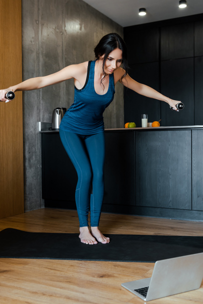 glückliche athletische Frau mit Kurzhanteln auf Fitnessmattentraining online mit Laptop - Foto, Bild