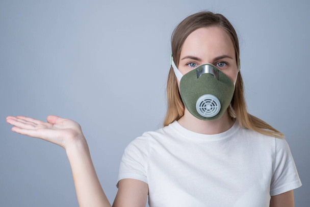 A woman in a respirator showing and presenting with open hand palm on a gray background. - Photo, Image