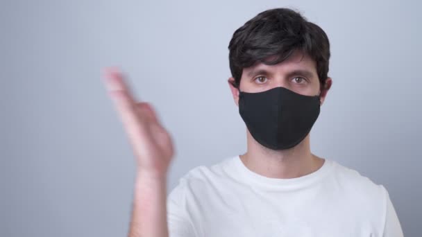 Man in a black medical mask showing and presenting with open hand palm on a gray background. - Filmmaterial, Video