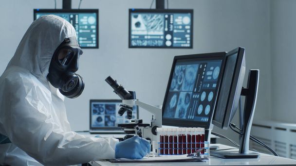 Tudós védőruhában és maszkban, laborban dolgozik laboratóriumi felszereléssel: mikroszkópok, kémcsövek. Coronavirus 2019-ncov veszély, gyógyszerészeti felfedezés, bakteriológia és virológia - Fotó, kép