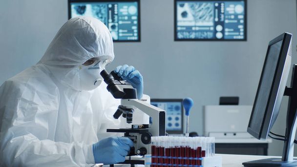 Scientist in protection suit and mask working in research lab using laboratory equipment: microscopes, test tubes. Coronavirus 2019-ncov hazard, pharmaceutical discovery, bacteriology and virology - Fotó, kép