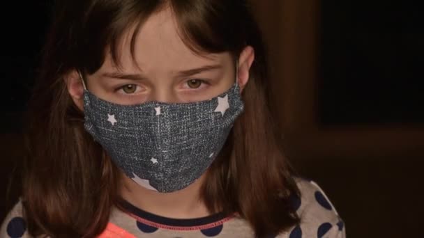 Egy kislány orvosi maszkban. Maradj otthon. Coronavirus vagy COVID-19. Aranyos lány védőmaszkban otthon egy szobában. Kislány orvosi maszkban otthon. 9 vagy 10 éves lány - Felvétel, videó