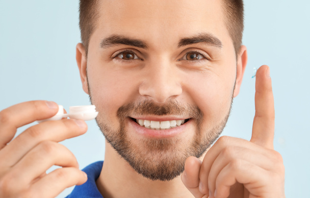 Young man with contact lenses on color background - Photo, Image