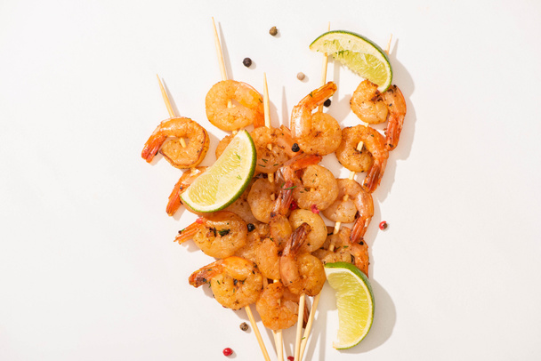 top view of prawns on skewers with lime and black pepper on white background - Zdjęcie, obraz