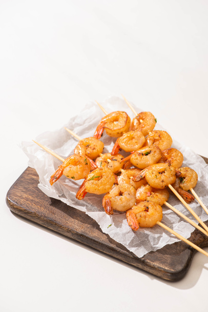 prawns on skewers on parchment paper on wooden board on white background - Фото, изображение