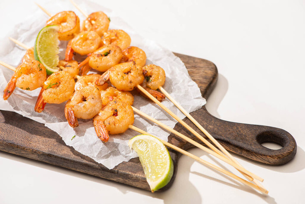 prawns on skewers with lime on parchment paper on wooden board on white background - Fotoğraf, Görsel