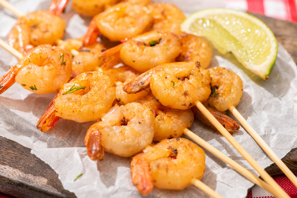 close up view of prawns on skewers with lime on parchment paper on wooden board - Фото, изображение