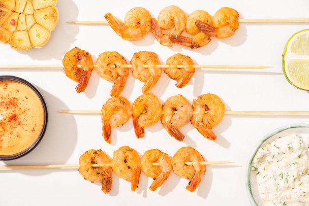 top view of delicious fried prawns on skewers with garlic, lime and sauces on white background - Photo, image