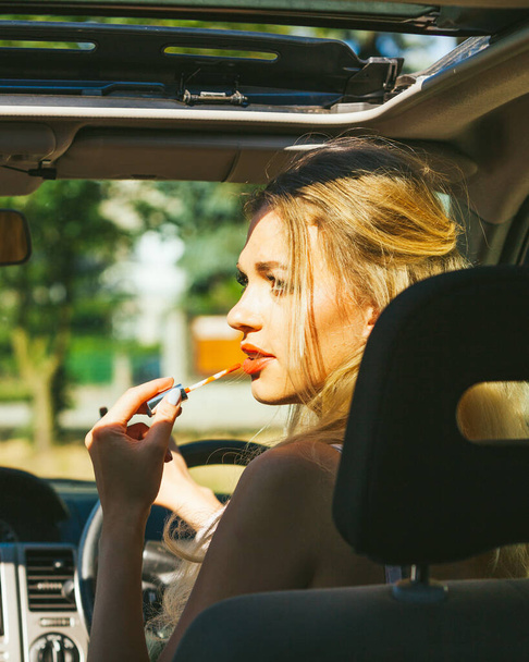 Concept of danger auto drive. Young woman driver painting her lips doing applying make up while driving the car. - Foto, Bild