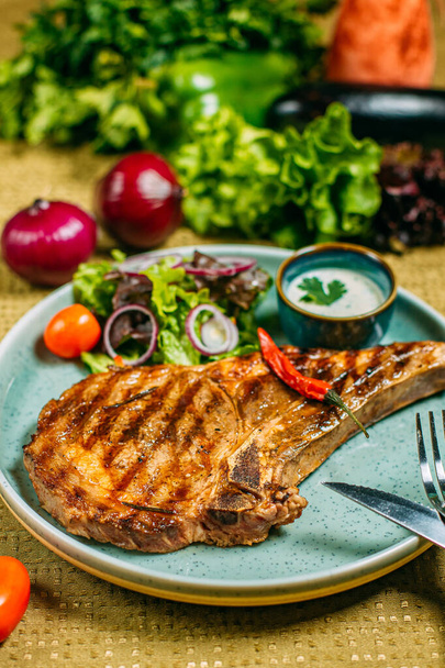 El bistec con hortalizas y la salsa en el plato, a la mesa adornada
 - Foto, imagen