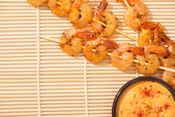 top view of tasty prawns on skewers with sauce on beige bamboo mat - Photo, Image