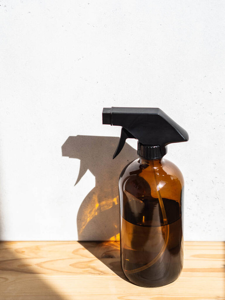 Kahverengi cam sprey şişesi ahşap rafta parlak arka planda - Fotoğraf, Görsel