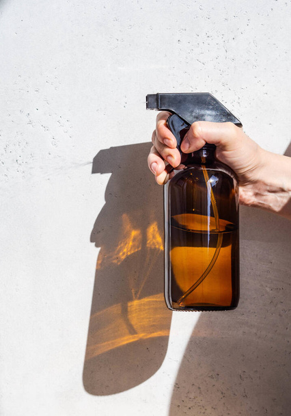 Frasco de spray de vidrio marrón en pulverizaciones manuales femeninas líquido sobre un fondo claro
 - Foto, imagen