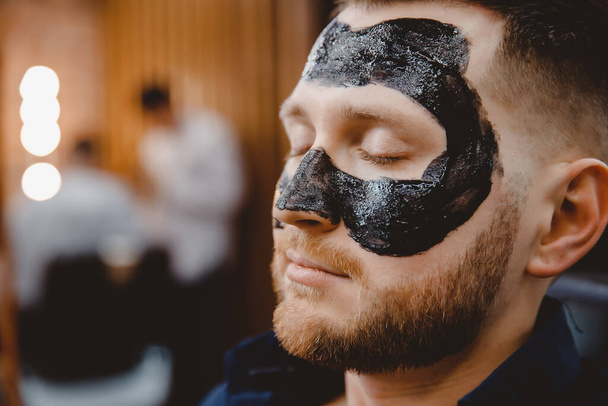 Akne poisto kosmeettisella valmisteella, puhdistus huokoset miesten ihon, parturi soveltamalla musta hiili naamio asiakkaan mies kylpylässä - Valokuva, kuva